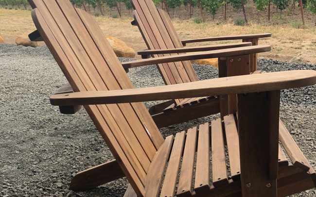 Two adirondack chairs with a view of the vineyard