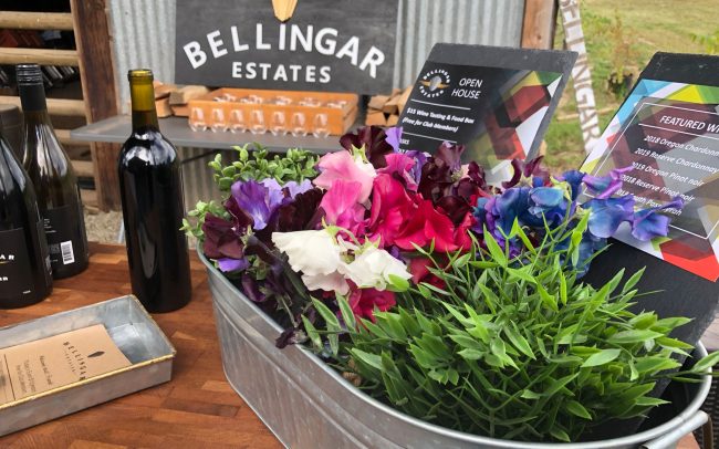 Table with a small flower bed, bottles of wine, and the Bellingar Estates sign